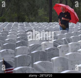 Un uomo che tiene un ombrello paga i suoi omaggi con una lapide sotto la pioggia il Memorial Day al Cape Canaveral National Cemetery. Foto Stock