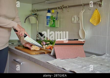 Metà della donna che prepara il cibo e guarda la compressa in cucina Foto Stock