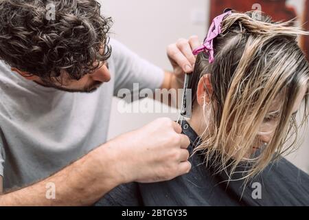 Il maestro parrucchiere taglia i capelli della donna bionda in salone. Primo piano della foto. Messa a fuoco selettiva. Foto Stock