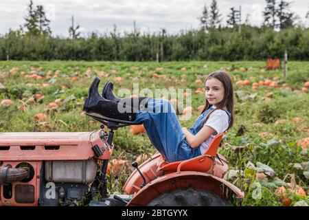 Giovane ragazza seduta sul trattore in un campo verde di fattoria. Foto Stock