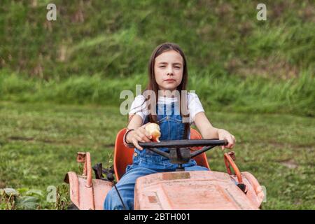 Giovane ragazza seduta sul trattore in un campo verde di fattoria. Foto Stock