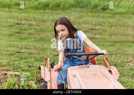 Giovane ragazza seduta sul trattore in un campo verde di fattoria. Foto Stock