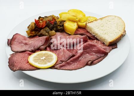 Affettare il manzo arrosto con patate e zucchine su un piatto bianco Foto Stock