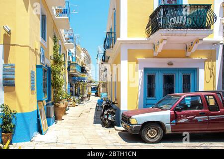 SYMI, Grecia - 27 giugno 2019: Via della città di Symi nell'isola della Grecia con le finestre blu e le porte di caffè, hotel e negozio e vecchia auto rossa Foto Stock