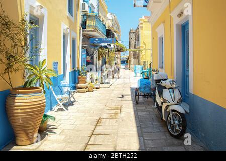 SYMI, Grecia - 27 giugno 2019: Via della città di Symi nell'isola della Grecia con le finestre blu e le porte di caffè, hotel e negozio e fiori pentole Foto Stock