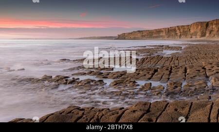 Acqua di mare, che si lava su una riva rocciosa, mentre il sole tramonta all'orizzonte. Una lunga esposizione ha creato un mare lattiginoso Foto Stock