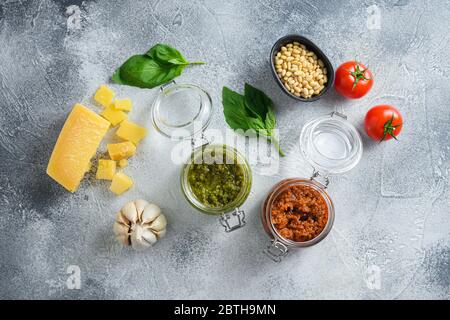 Pesto vegetariano fatto in casa pesto normale e pesto rosso e ingredienti da cucina Parmigiano, foglie di basilico, pinoli, olio d'oliva, aglio, sale, pepe Foto Stock