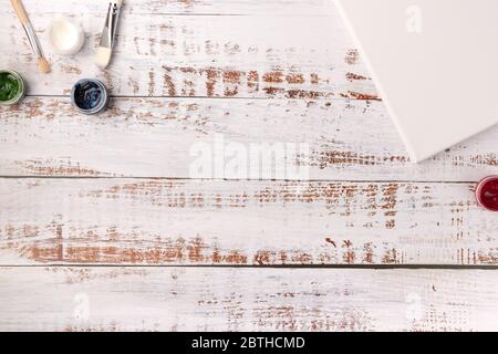 Tavola creativa colorata con tela vuota per schizzi e vernici, pennelli su tavolo in legno bianco, vista dall'alto, spazio copia, stile piatto, driwi Foto Stock