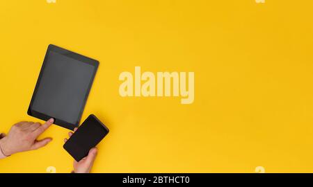 Primo piano su mani uomo appeso cellulare e tablet su sfondo giallo, Foto Stock