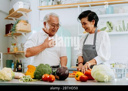 Senior Asian sposato cucina cibo in casa. Anziani anni '70 uomo e donna preparare insieme gli ingredienti in cucina. Foto Stock