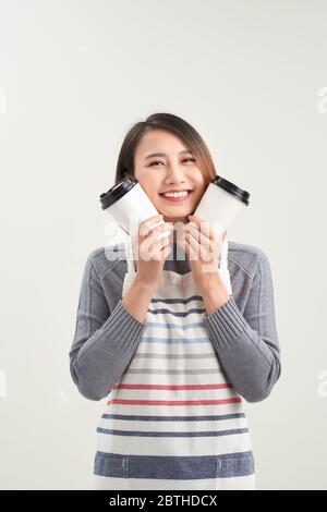 La ragazza affascinante tiene una tazza usa e getta con bevande e guarda direttamente alla macchina fotografica isolata su sfondo bianco Foto Stock