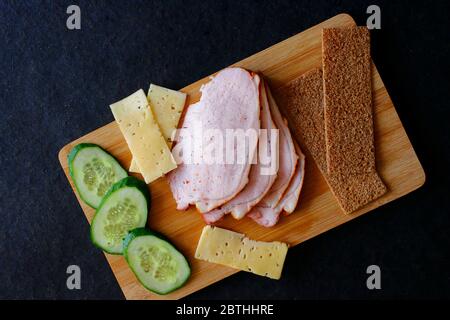 Affettare prosciutto di carne, cetrioli, formaggio e pane ruddy su un asse di legno. Vista dall'alto Foto Stock