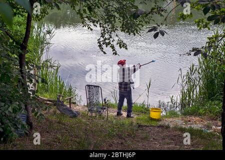 Un pescatore dilettante di sport prova a gettare il cibo il più lontano possibile dalla riva. In questo modo, nel fiume cercando di attirare il pesce. Foto Stock