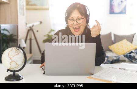 Donna di mezza età lavora a casa con un computer - donna in videochiamata con cuffie Foto Stock