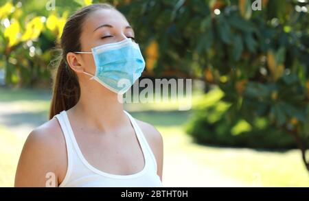 COVID-19 primo piano di una giovane donna sportiva con maschera chirurgica che respira nel parco Foto Stock