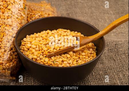 Piselli spezzati gialli in sacchetto di cellofano e cereali in una ciotola di ceramica su sfondo di tela ruvida. Cereali tradizionali per la preparazione di zuppe Foto Stock