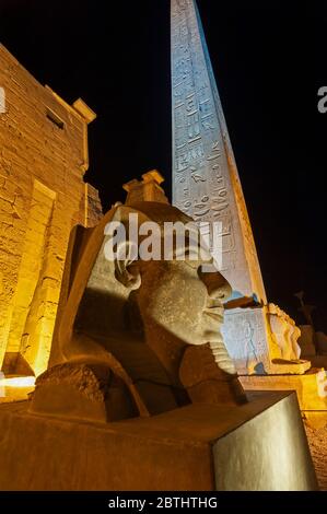 Grande statua testa del faraone Ramses II durante la notte presso l'antico tempio egiziano Luxor con obelisco illuminato in background Foto Stock