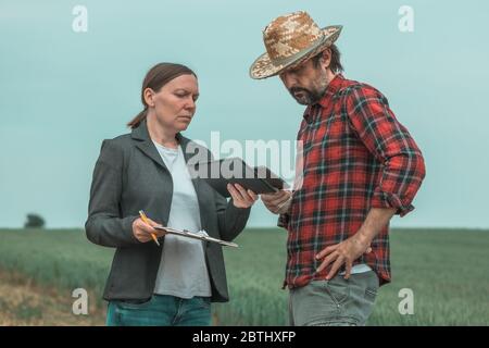 Banchiere e agricoltore che negoziano prestiti bancari per l'agricoltura in campo di grano verde, fuoco selettivo Foto Stock