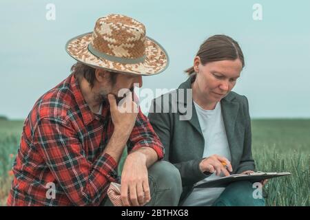 Banchiere e agricoltore che negoziano prestiti bancari per l'agricoltura in campo di grano verde, fuoco selettivo Foto Stock