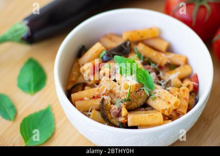 Piatto tradizionale italiano: Pasta alla norma con pomodori, melanzane, aglio, basilico e ricotta su un tagliere in legno Foto Stock