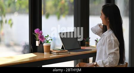 Donna di affari che allunga la sua mano mentre si siede e si rilassa davanti al suo tablet del computer con schermo nero vuoto che mette su bancone bar di legno Foto Stock