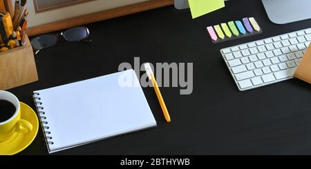 Foto di un'area di lavoro ordinata, Nota e penna che si trova su una scrivania nera e circondata da una tazza da caffè, cornice, stazionaria nel portamatite, wirel Foto Stock