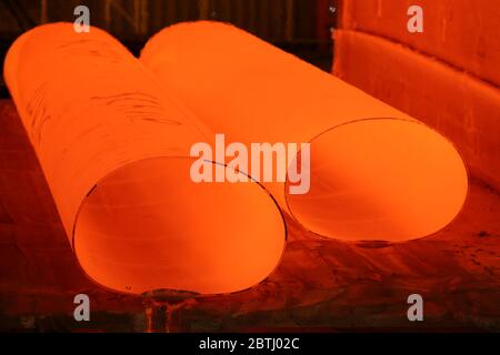 Grandi tubi di acciaio rosso caldo che escono dal laminatoio e formatore Foto Stock