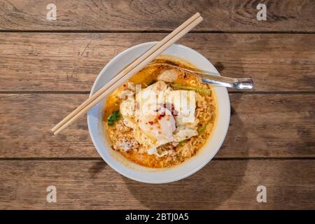 Vista dall'alto dei tagliatelle tom yum con carne di maiale tritata e uova fritte su un tavolo di legno Foto Stock