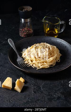 Cacio e Pepe - Pasta Italiana con formaggio e pepe su piatto nero su sfondo scuro. Foto Stock