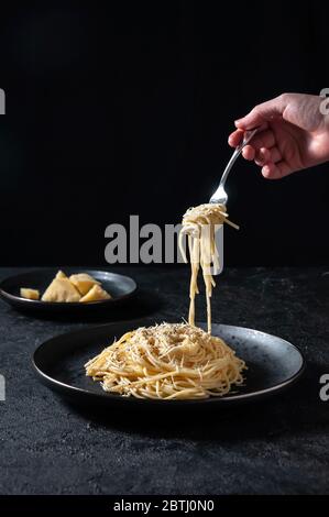 Cacio e Pepe - Pasta Italiana calda con formaggio e pepe su piatto Nero, Forchetta Donna con spaghetti su sfondo scuro. Foto Stock