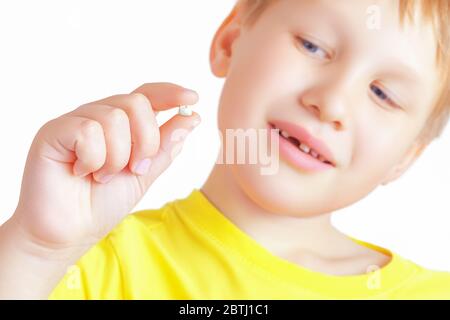 Piccolo ragazzo caucasico carino tiene in mano il primo dente di latte caduto e lo guarda. Foto Stock