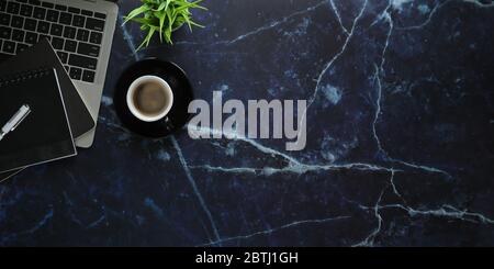 Immagine dall'alto della tazza da caffè che si trova su una scrivania in marmo circondata da computer portatile, blocco di notebook, caffè, penna e vasetto Foto Stock