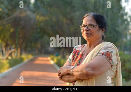 Donna indiana del nord intelligente e sicura in piedi, pensando e guardando via con le mani incrociate / ripiegate in un parco che indossa una vera e propria salwar Foto Stock