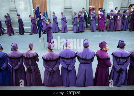 Gli uomini in abiti viola si allineano davanti ai marchers processionisti che portano il galleggiante di Cristo un mese prima di Pasqua. Quetzaltenango, Guatemala. Mar 2019 Foto Stock