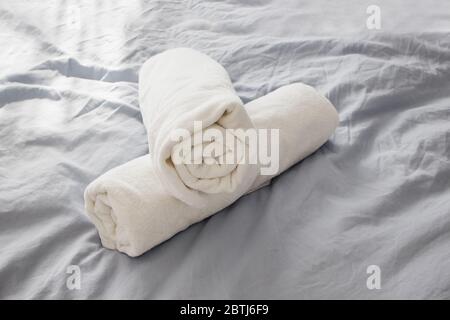 Asciugamani bianchi e puliti sul letto con lenzuola grigie. Foto Stock