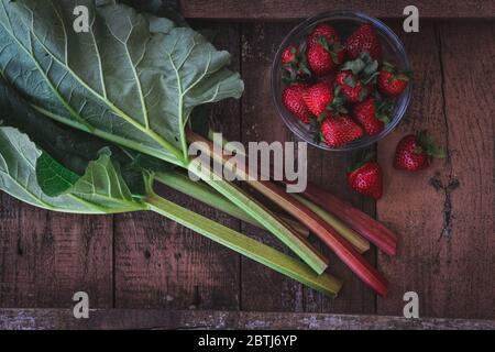 Gambi di rabarbaro e fragole su un tavolo da giardino scuro Foto Stock
