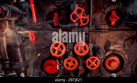 Foto tonica di vecchi tubi di vapore arrugginiti e valvole rosse sulla caldaia a vapore della vecchia locomotiva Foto Stock