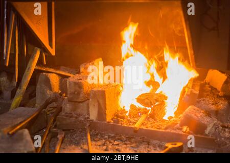 Un fuoco che brucia nel forno a forgiare, workshop. Fabbro attrezzature concept Foto Stock