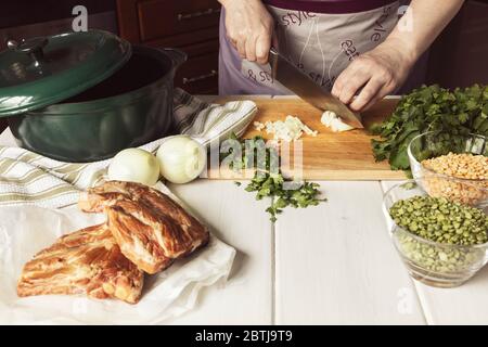 Cottura di zuppa di piselli spezzati essiccati con costolette di pok. Donna taglia cipolle ed erbe. Foto Stock