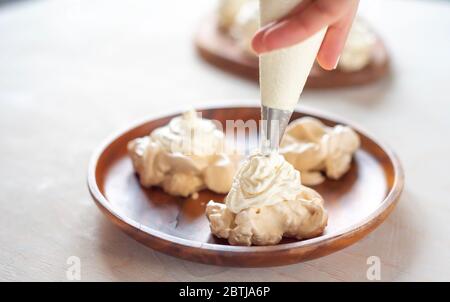 Il processo di creazione di Pavlova dessert, decorazione della meringa con crema dalla borsa culinaria Foto Stock