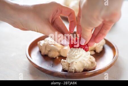 Il processo di creazione di Pavlova dessert, decorazione della meringa con crema dalla borsa culinaria Foto Stock