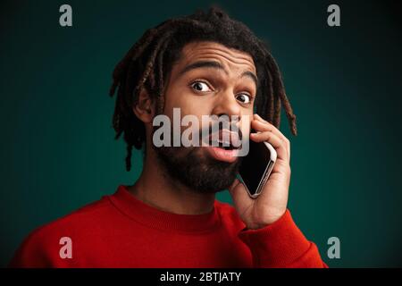 Ritratto di afroamericano che esprime sorpresa e utilizzando cellulare isolato su sfondo verde Foto Stock