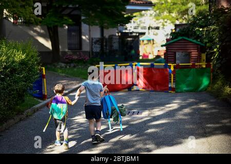 Ivrea, Italia - 26 maggio 2020: Due bambini entrano in un giardino scolastico che tiene le mani. Il comune di Ivrea apre i giardini di due scuole di asilo come parte di un test pilota per vedere come le scuole possono riaprire dopo il blocco del coronavirus COVID-19. Credit: Nicolò campo/Alamy Live News Foto Stock