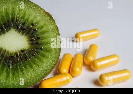 Integratore di vitamine nutrizionali: Macro primo piano di kiwifuit verde maturo isolato a metà fette con capsule gialle di pile Foto Stock