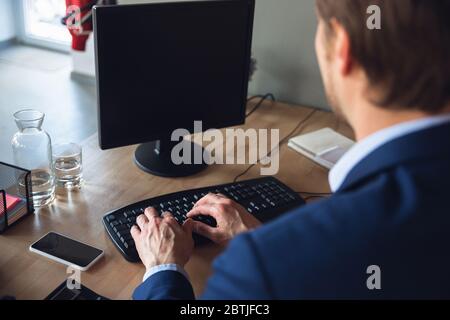 Digitazione del testo, lavoro, risposta attenta. Giovane uomo, manager torna al lavoro nel suo ufficio dopo la quarantena, si sente felice e ispirato. Tornare alla vita normale. Business, finanza, emozioni concetto. Foto Stock