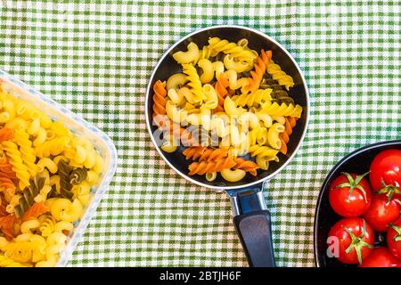 Piccola padella con fusilli tricolore crudo in una composizione rustica. Foto Stock