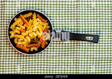 Piccola padella con fusilli tricolore crudo in una composizione rustica. Foto Stock