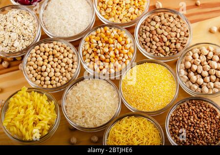 Vista piatta su set di legumi e grani vari in ciotole di vetro su tavola di legno da cucina, non deperibile, concetto di cibo a lunga durata di conservazione Foto Stock