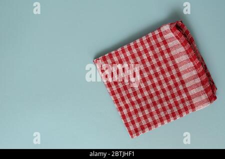 Sfondo turchese chiaro con un asciugamano rosso da cucina. Asciugamani o tovaglioli piegati a scacchi in lino. Background multitasking minimalistico. Vista dall'alto. Foto Stock