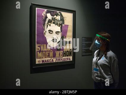 Un dipendente che indossa una maschera facciale e uno scudo protettivo è visto guardando un dipinto della mostra 'rompere il silenzio. Il film silenzioso in Russia durante la fase 1 al Museo russo di San Pietroburgo.Spagna sta attraversando un piano di riduzione verso una 'nuova normalità', rilassando le misure di epidemia di COVID-19. Diversi importanti musei della città di Malaga hanno riaperto dopo l'inizio dello stato di emergenza, garantendo misure di sicurezza come maschere facciali, disinfettanti, scansioni di temperatura all'ingresso dei musei. Foto Stock